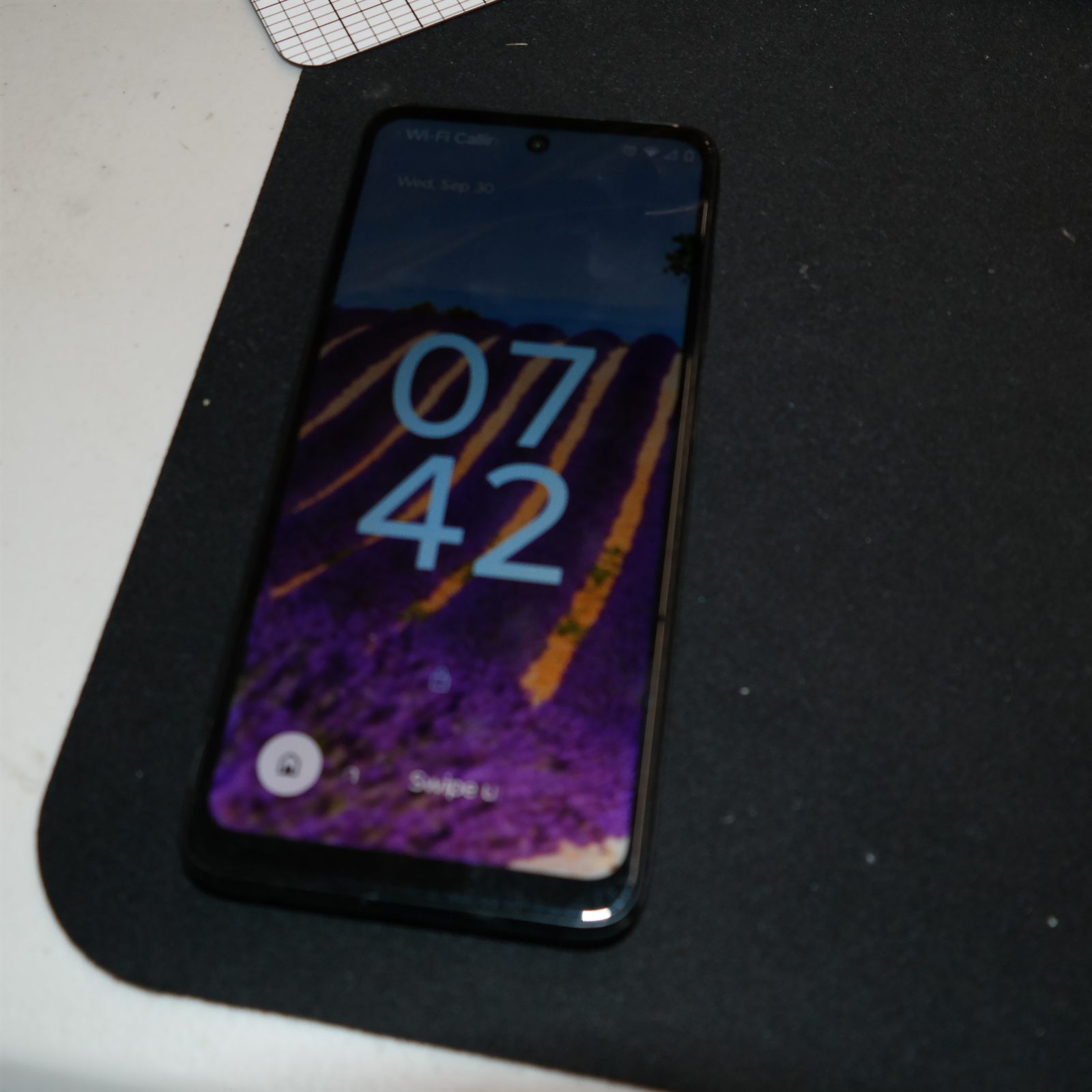 The reassembled Moto G 5G (2022) lying face up on a black repair mat, powered on and showing its lock screen with the clock, date and a lavender-field wallpaper. The rear cover sits flush against the frame.